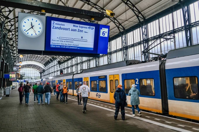 Crowds of people wearing rain gear walk, cycle, and ride the bus and train during the Dutch Grand Prix on a rainy day in Zandvoort.