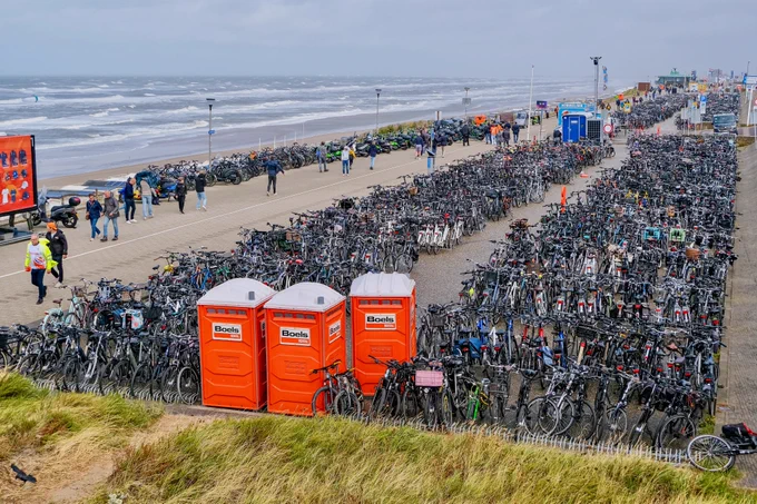 Crowds of people wearing rain gear walk, cycle, and ride the bus and train during the Dutch Grand Prix on a rainy day in Zandvoort.