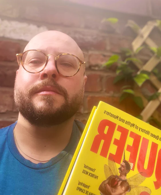 Bald man with book by a brick wall