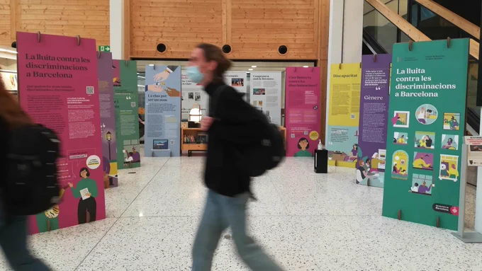 Una persona creua per davant dels plafons de l'exposició "La lluita contra les disciminacions a Barcelona".