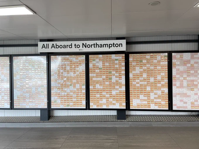 A wall that says “All aboard a to Northampton” with lots of tickets in cases but spaces between them with missing tickets.
