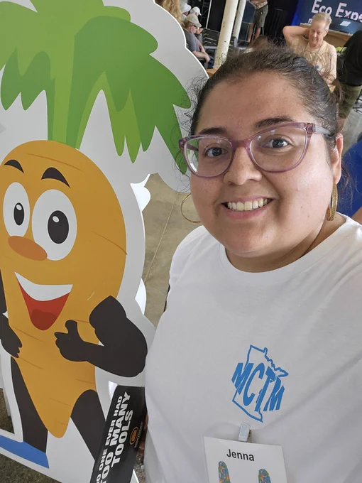 Selfie of Jenna next to a carrot wearing a white tshirt with the letters MCTM in blue