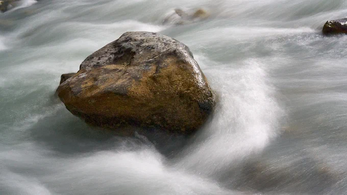 A long exposure showing water rushing around the edge of rock in Wildcat Creek. As the flow shapes around the rock, foam builds up in the highest flow areas.