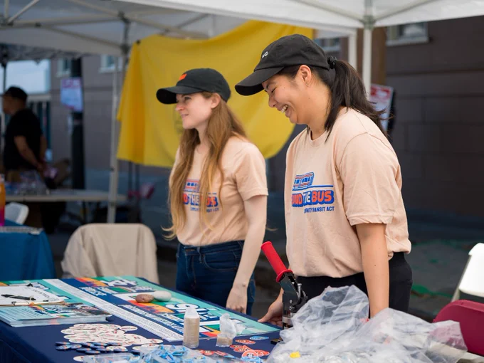 Two volunteers laughing behind a table with colorful literature and swag.