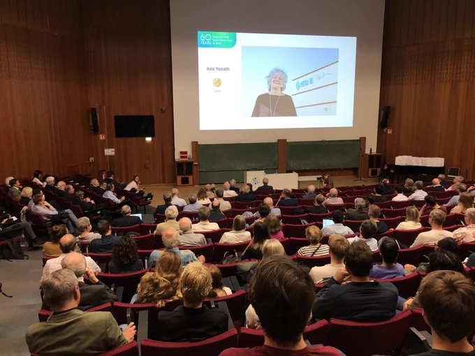 Ein voller Hörsaal mit einer Präsentation, die eine Frau mit dem Namen "Ada Yonath" zeigt