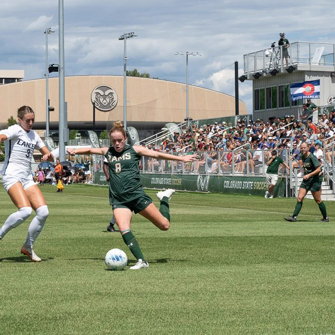 C S U soccer player Kacie Laurie kicking the soccer ball during the game. Packed stands and the new soccer complex can be seen in the background.