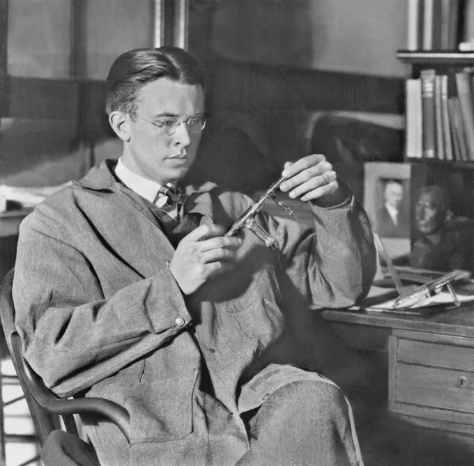 Ernest Orlando Lawrence sitting in a chair with the cyclotron in his hands. 