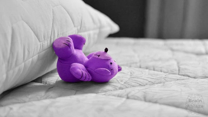 A purple teddy bear lays on a black-and-white bed. 