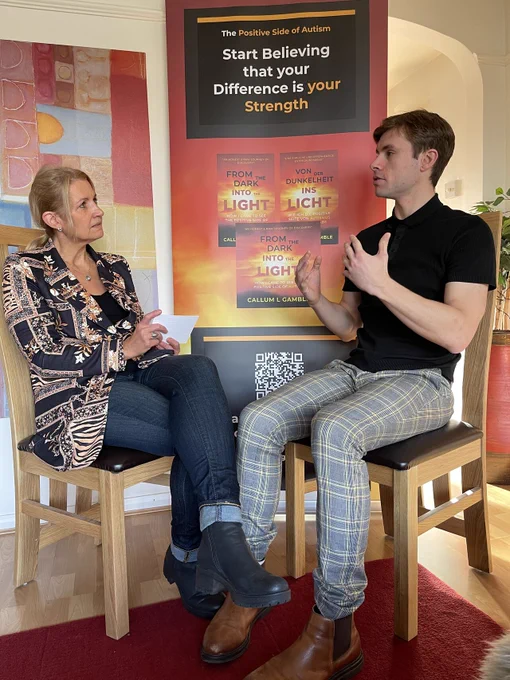 Callum and Caren sat down in front of their roller banner. Caren is interviewing Callum. She has prompts in her hands while Callum is answering the questions.
