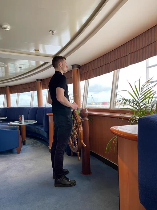 Callum stood up, holding a steering wheel in a bar on a ferry from Hull to Rotterdam.