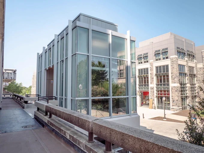 Glass and precast elevator tower connecting to the second floor landing at Derring Hall. Grey Hokie Stone Hitt Hall is in the distance. 