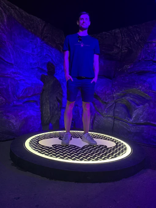 Callum stood on a platform at the Batman Unmasked Exhibition in Manchester, United Kingdom. The platform has a Batman logo on it.