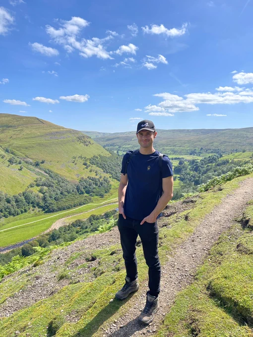 Callum stood on top of the hills, on a sunny day, in the Yorkshire Dales on the Muker trail.