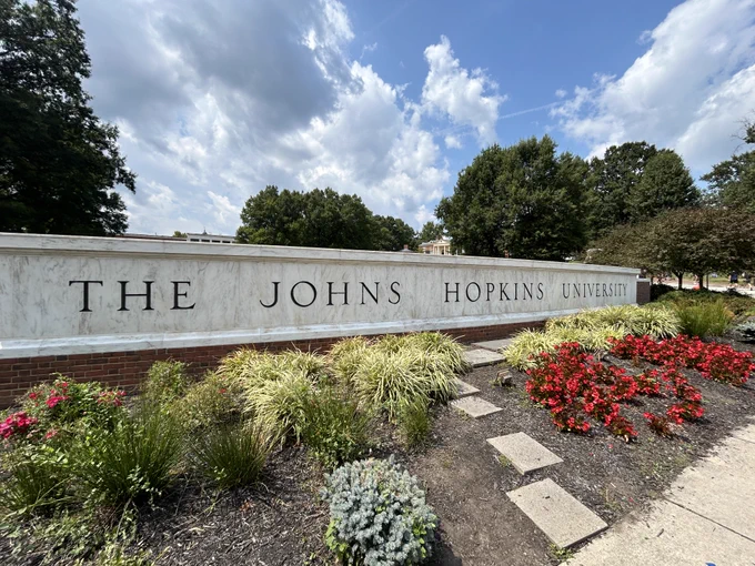 The Johns Hopkins University front entrance sign on the Homewood campus surrounded by plants and flowers.