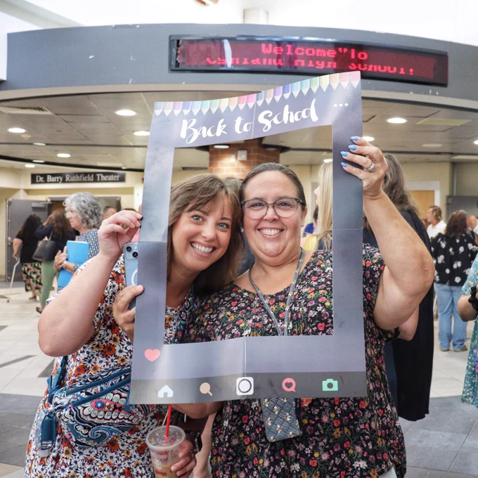 Two staff members smile behind large-scale, paper Back to School Instagram frame