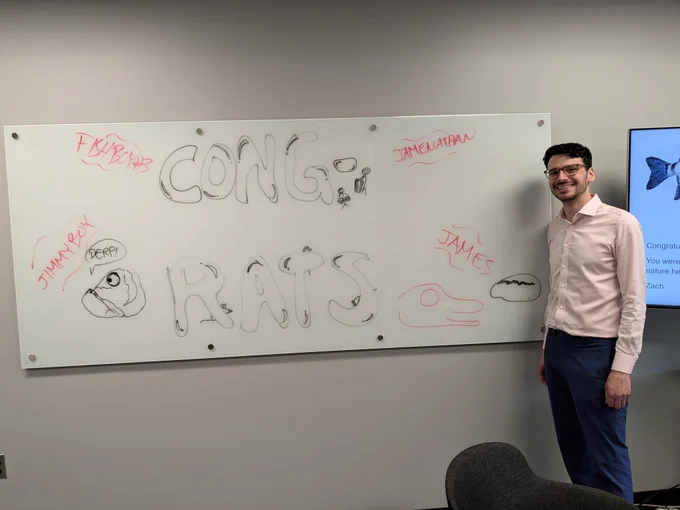 James in front of a whiteboard with a congratulatory note.