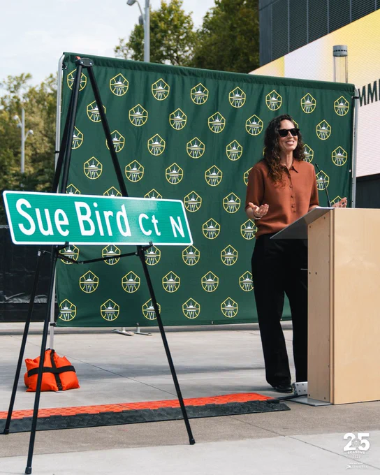 Sue Bird standing at a podium next to a replica Sue Bird Ct street sign