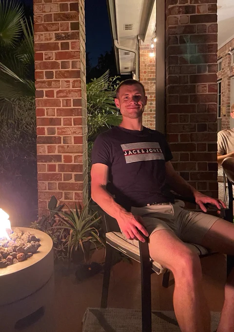 Callum is sat in front of a fire in the garden at night time.