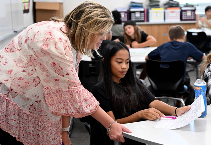 An educator assisting a student with schoolwork in a classroom setting.