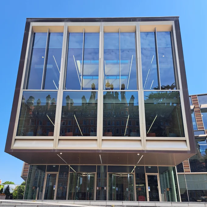 The front of the Emily Wilding Davison building on a sunny day. It has large windows in which the Founder's Building can be seen in reflection.