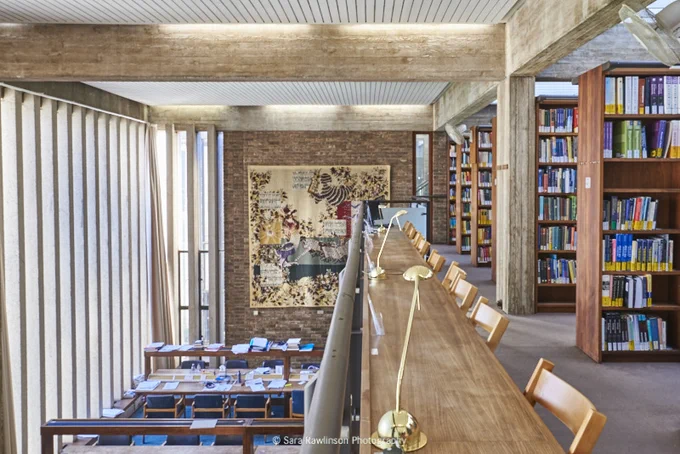 View from the top of the Bracken Library Gallery. On the upper floor, bookcases and a row of desks overlooks desks below. A large tapestry hangs on the far wall.