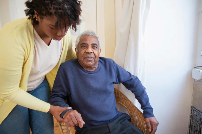 A woman helping an elderly man up from a chair
