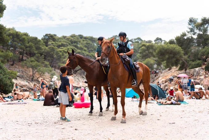 Enfant caressant le cheval des gendarmes sur une plage.