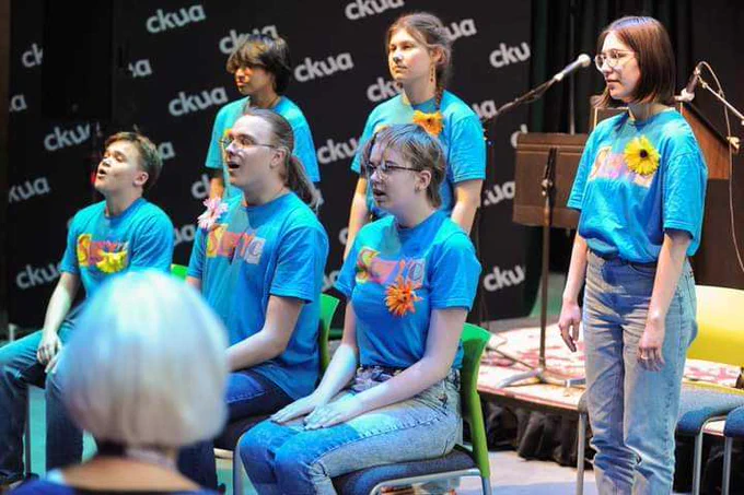 Members of the Spoken Word Youth Choir sit and stand in two rows during a performance. Photo Credits: Alexis Marie Chute/Edmonton Poetry Festival.