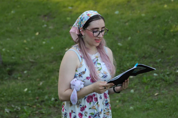 A camper stands in the grass outside, reading a poem from their notebook. 