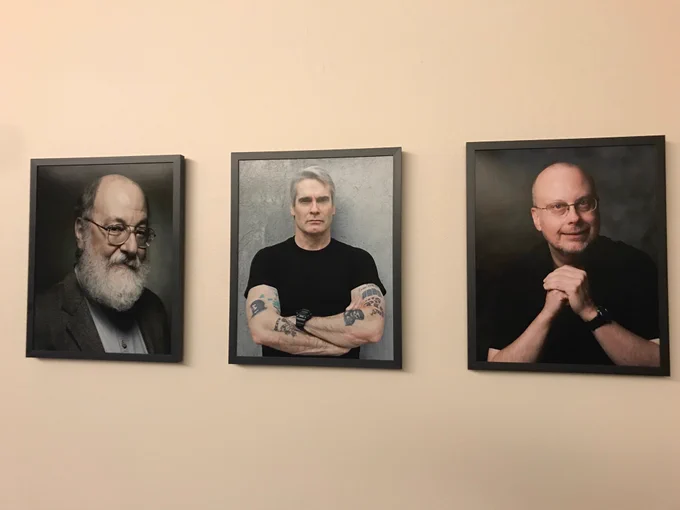 Framed photos of Harry Turtledove, Henry Rollins, and Robert J. Sawyer hang on an otherwise bland an uninspiring office wall.