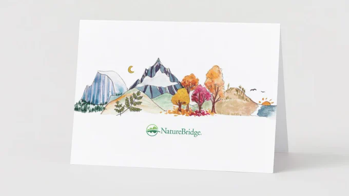Photo of a greeting card with a hand-drawn design depicting mountains, trees, and Half Dome with the NatureBridge logo at the bottom