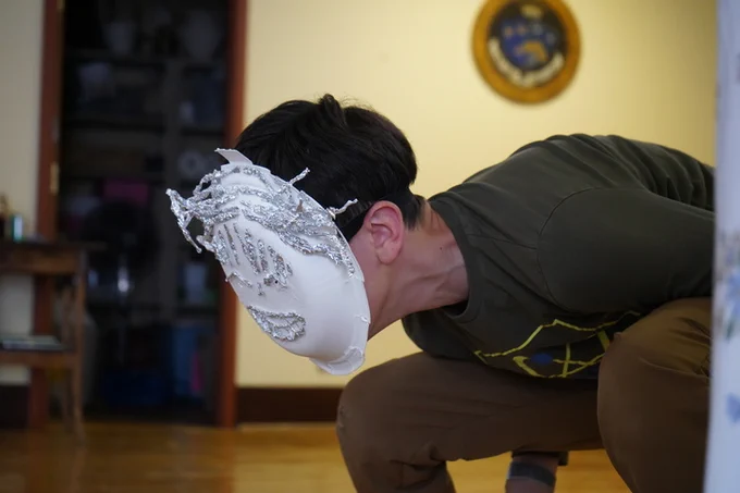 A camper crouches and leans forward, wearing a paper plate mask decorated with tin foil facial features. 