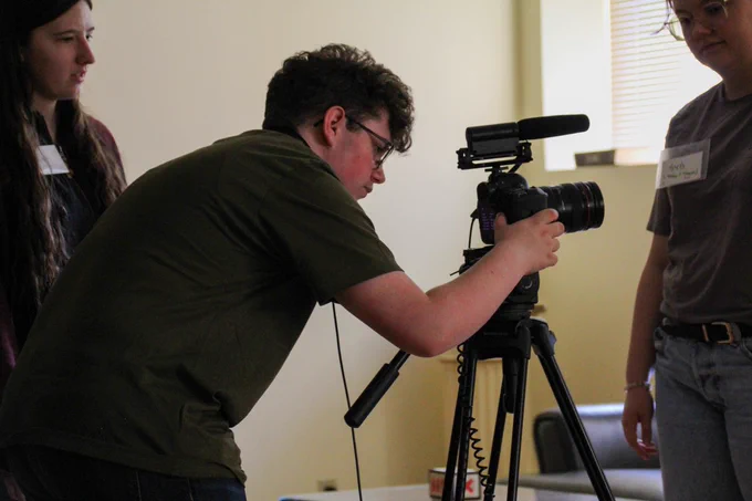 A camper looks into a video camera on a tripod stand, pointing to the right. 