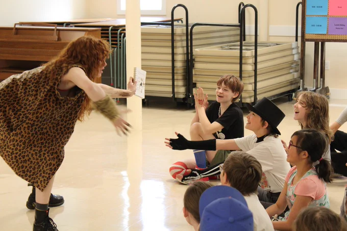 Campers clap and cheer while sitting on the floor, watching  Thoog the Caveman perform. 