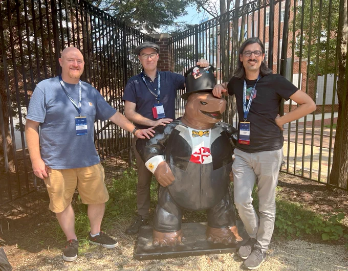Our Sr Drupal Architect, Bob McDonald, Sean and Andrew stand in the mottled sunlight around a statue of a turtle dressed in a tuxedo and top hat.  The terrapin turtle is the mascot of the University of Maryland where GovCon took place.