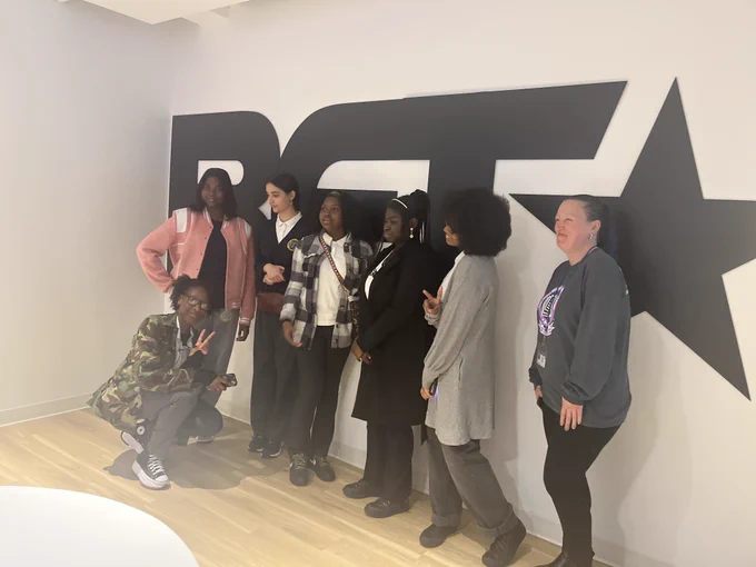 Students and a teacher pose in front of a wall with the BET logo on it. 