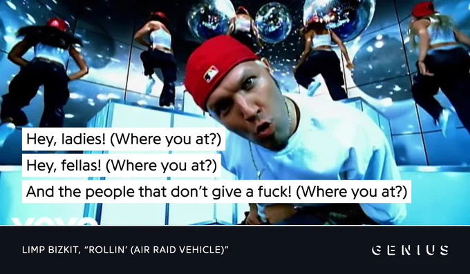 A screenshot from the music video for Limp Bizkit's "Rollin' (Air Raid Vehicle)". Frontman Fred Durst, in his signature backwards red hat and white t-shirt, mugs at a fisheye lens. Backup dancers are in the background in similar outfits. A lyric caption reads: "Hey, ladies! (Where you at?) / Hey, fellas! (Where you at?) / And all the people that don't give a fuck! (Where you at?)"