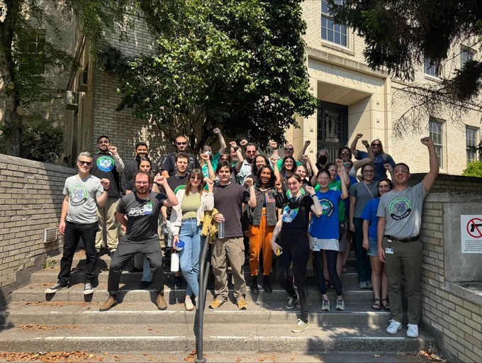 ONA members standing with and supporting OHSU postdocs, group photo outside on concrete steps with fists raised in the air. 