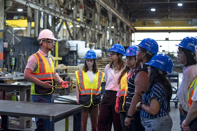 Students visit a factory and wear construction hats. 