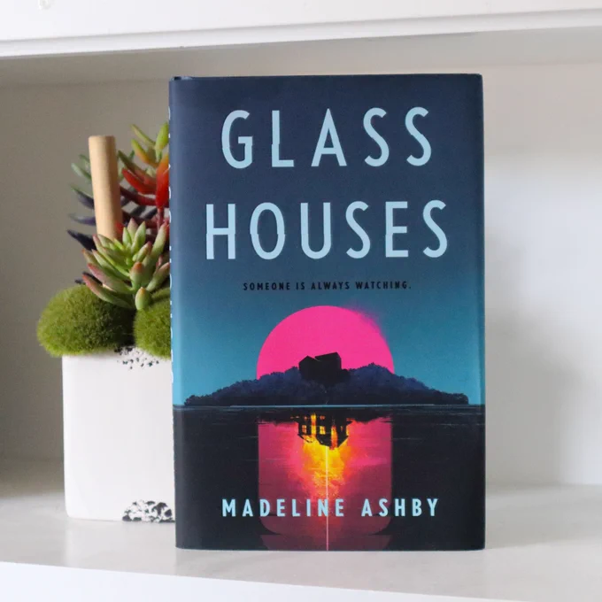 Glass Houses by Madeline Ashby is standing on a white surface beside a house plant 