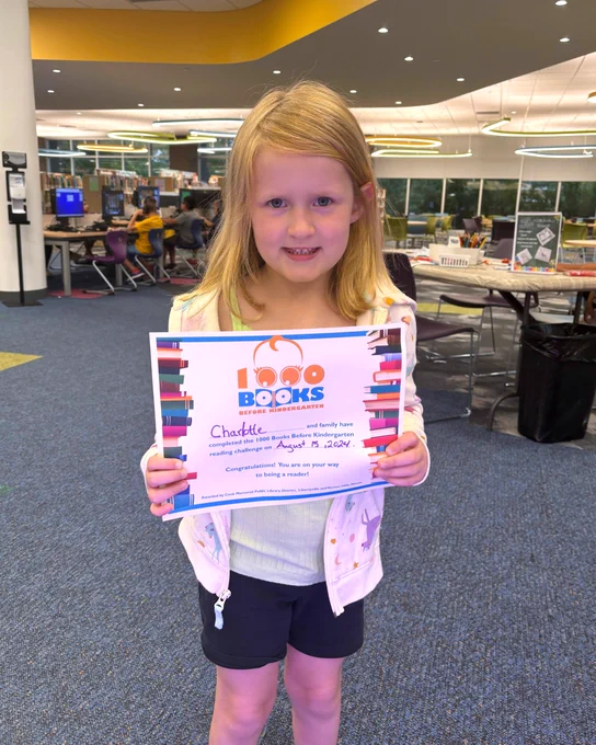 photo of a young girl holding up a certificate stating she completed the library's 1000 books before kindergarten reading program.