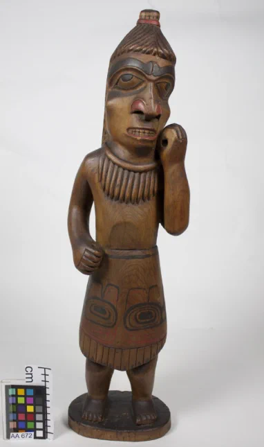 Wooden sGaaga, full body, brown with black and red details, left hand raised to cheek
