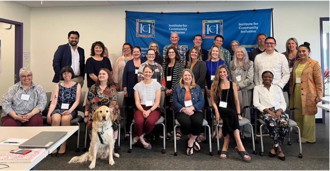 A diverse group of people sitting and standing in front of a banner with ICI logos on it. Everyone is posing for the photo and smiling at the camera. 
