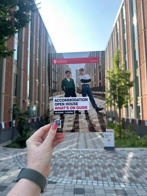 A hand with pink nail polish is holding up a booklet called "Accommodation open house what's on guide". In the background are the tower blocks of The City accommodation.