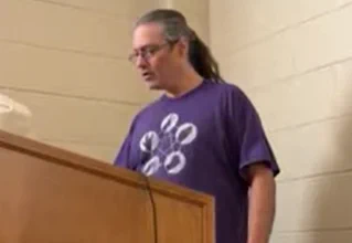 Photo of Sean wearing a purple shirt, looking down at a lectern.