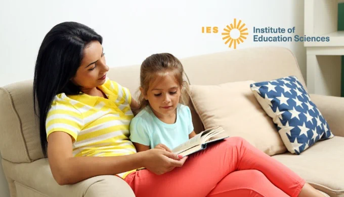 A mother and young daughter sitting together reading on a sofa with the Institute of Education Sciences (IES) logo.