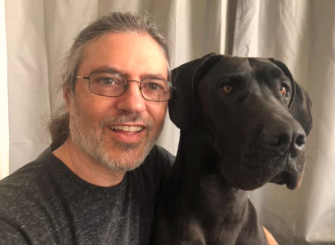 Photo of Sean and a big black dog - a Great Dane - looking off past the camera.