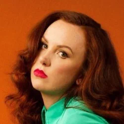 A red-headed woman looks directly at the camera