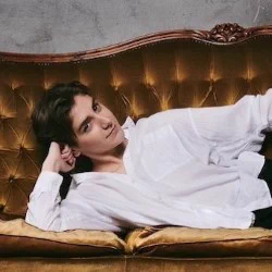 A non-binary person reclines on a chaise longue