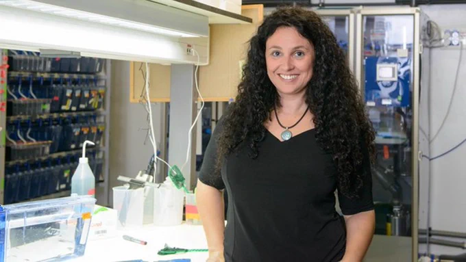 Image of Prof. Karina Yariv standing in front of a bench and zebrafish racks